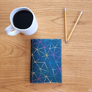 May include: A dark blue notebook cover with a geometric pattern of colorful lines. The cover has a subtle sheen and is made of a durable material.