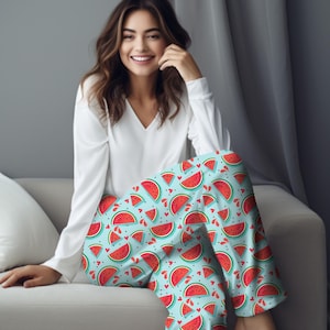 Può includere: Pantaloni da pigiama azzurri con un motivo a fette di anguria. I pantaloni presentano fette di anguria rosse con semi neri e bucce verdi, insieme a piccoli cuori rossi, su uno sfondo azzurro. La persona indossa una camicia bianca a maniche lunghe.