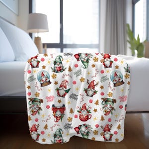 May include: White throw blanket featuring a repeating pattern of gnomes wearing red, green and white hats. The gnomes are holding various Christmas-themed items, such as candy canes, snow globes and Christmas trees. The background is white with gold stars, red and white candy canes and green sprigs.