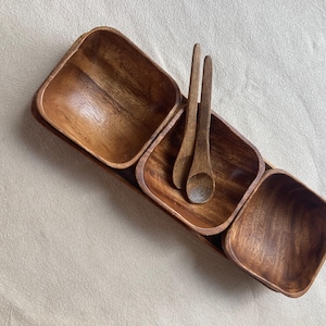May include: A wooden serving tray with three separate compartments and two wooden spoons. The tray is made of light brown wood and has a natural finish.