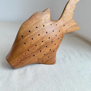 May include: A wooden fish-shaped trinket with a brown finish and a pattern of small holes throughout the surface.