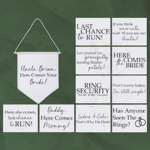 May include: A set of nine white signs with black text for a wedding. The signs have various wedding-themed messages, such as "Here Comes the Bride", "Last Chance to Run", and "Ring Security".