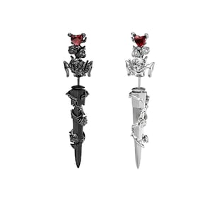May include: A pair of earrings with a black and silver finish. Each earring features a rose design with a red heart-shaped gem at the top. The earrings are in the shape of a dagger with a vine design.
