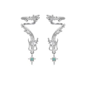 May include: A pair of silver-colored ear cuffs. Each cuff features a dragon design that wraps around the ear, with a turquoise-colored star pendant dangling below. The dragon's head is detailed, and the overall design is intricate.