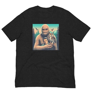 May include: A black t-shirt with a graphic of a large, furry creature with a man and an owl. The creature is brown and has a large, white beard. The man is wearing a blue shirt and has brown hair. The owl is brown and white and has large, yellow eyes.