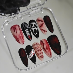 May include: A set of ten press-on nails in a clear plastic case. The nails feature a variety of designs, including a bloody slash, a ghost face, and the text "WHAT'S YOUR FAVORITE SCARY MOVIE?" in red.