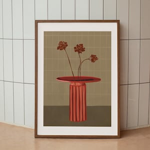 Op de afbeelding: Een ingelijste kunstdruk met een rode, gestileerde vaas met drie bruine bloemen. De vaas heeft een ronde bovenkant en een geribbelde, cilindrische basis. De achtergrond is een rasterpatroon in groen- en bruintinten.