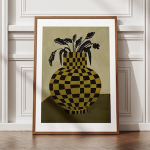Könnte beinhalten: Gerahmter Kunstdruck mit einer stilisierten Vase mit einem schwarz-goldenen Schachbrettmuster. Die Vase enthält schwarze Pflanzensilhouetten vor einem gedämpften grünen Hintergrund. Das Kunstwerk wird in einem Raum mit weißen Leisten und Holzboden ausgestellt.
