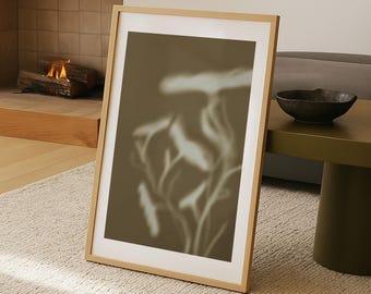Op de afbeelding: Een ingelijste kunstdruk met een vage botanische vormgeving in wit- en bruintinten. Het kunstwerk wordt gepresenteerd in een licht houten frame met een witte passe-partout. De print leunt tegen een muur op een beige tapijt.