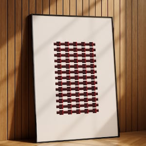 May include: Framed abstract art print featuring a geometric pattern of alternating dark red and maroon rectangles with thin red lines. The artwork is set against a cream background and framed in black. The print is leaning against a wooden wall.