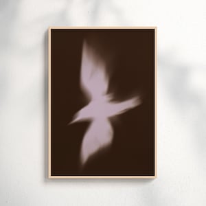 May include: A rectangular wall art print in a light wood frame featuring a blurred, soft-focus silhouette of a bird in flight. The bird is rendered in a pale, muted lavender tone, set against a solid, deep dark brown background.
