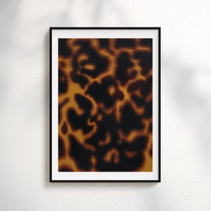 Pode incluir: Uma impressão de arte emoldurada com um close-up de um padrão de casco de tartaruga. O design apresenta uma mistura de tons castanhos escuros e âmbar, criando uma estética natural e orgânica. A impressão está dentro de uma moldura preta com uma borda branca.