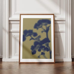 Può includere: Una stampa artistica incorniciata con un'immagine sfocata di rami floreali blu su uno sfondo dorato tenue. L'opera d'arte è presentata in una cornice di legno marrone, che aggiunge calore. La stampa è un elemento decorativo.