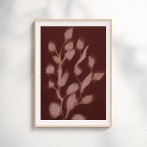 May include: A framed botanical print featuring a soft, blurred image of plant stems and leaves in shades of pink and white against a deep burgundy background. The artwork is encased in a light-colored wooden frame.
