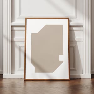 Puede incluir: Una impresión abstracta enmarcada con una forma geométrica beige sobre un fondo blanco. El marco es de madera marrón claro.