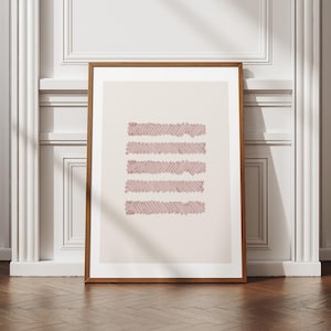 May include: A framed art print featuring five horizontal, textured, maroon-colored lines on a cream background. The artwork is displayed in a brown wooden frame and leans against a white wall and a wooden floor.