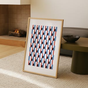 Op de afbeelding: Een ingelijste kunstdruk met een geometrisch patroon van herhaalde blauwe, rode en zwarte rechthoeken. Het kunstwerk wordt gepresenteerd in een licht houten frame. De print leunt tegen een muur. Het ontwerp heeft een moderne en minimalistische uitstraling.
