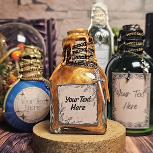 May include: A collection of decorative potion bottles with ornate details. The central bottle is gold with a label that reads "Your Text Here." Other bottles are blue and green, with various embellishments. A book with the text "IN THE DARK of NIGHT" is in the background.