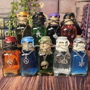 May include: A collection of decorative glass bottles with colorful liquid contents. Each bottle has a unique wax seal, twine, and a pendant necklace. The bottles are arranged on a wooden surface, with books and decorative items in the background.