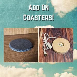 May include: The image showcases two coaster options. One is a dark gray, round slate coaster. The other is a round, wooden base with a USB cable and a small light inside. Text at the top reads "ADD ON COASTERS!"