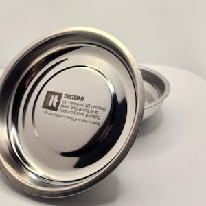 May include: Two stainless steel magnetic trays. The larger tray has the text "CUSTUM IT" and "On demand 3D printing, laser engraving and custom t-shirt printing." The trays are on a white surface.
