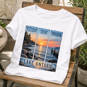 Peut inclure: Un t-shirt blanc avec une impression graphique divisée en trois panneaux verticaux montrant un coucher de soleil sur le lac Ontario. Le texte YESTERDAY, TODAY, TOMORROW est imprimé au-dessus et LAKE ONTARIO est imprimé en dessous.