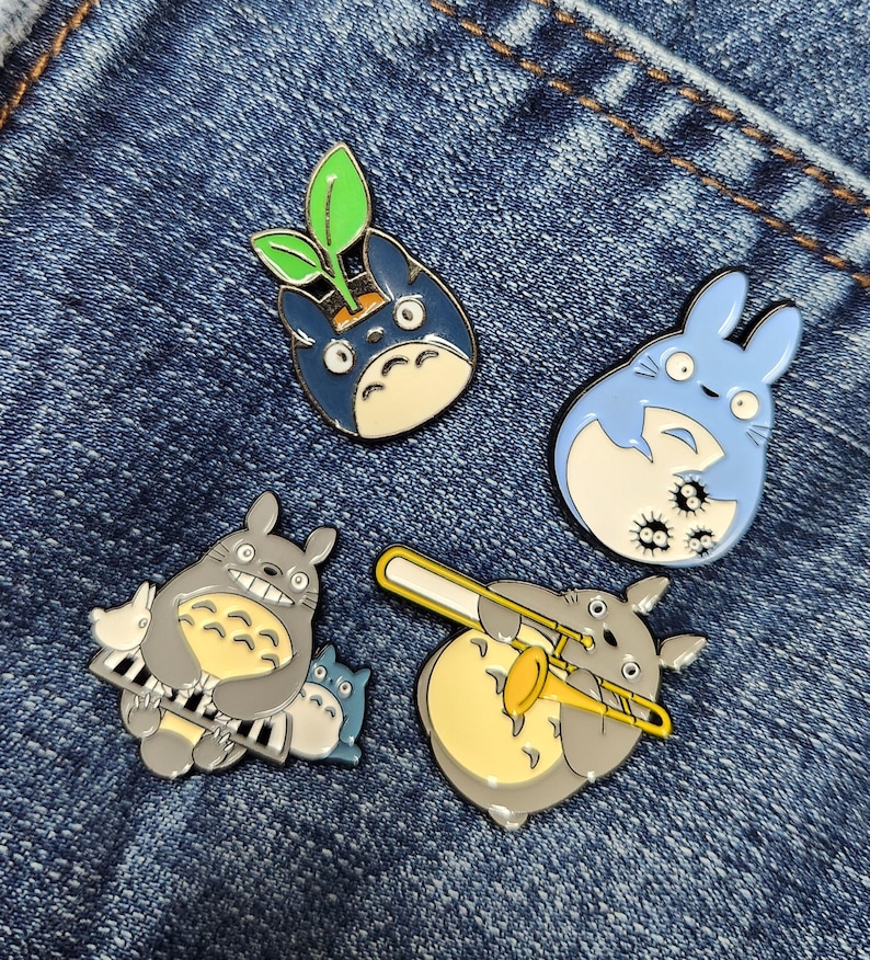Puede incluir: Cinco pines de esmalte con un personaje de dibujos animados con ojos y orejas grandes. Los pines est&aacute;n en varias poses, incluyendo tocando un tromb&oacute;n, sentado en un piano y con una planta que le crece de la cabeza. Los pines est&aacute;n sobre un fondo de mezclilla azul.