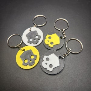 May include: Four keychains with a skull design. Two keychains are black with a white skull, one keychain is yellow with a black skull, and one keychain is white with a black skull.