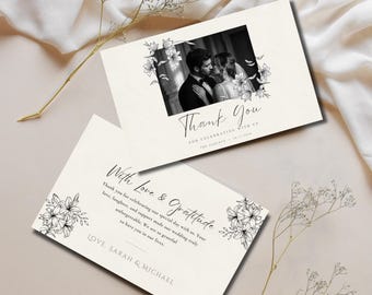 May include: Two off-white rectangular wedding thank you cards featuring black ink floral illustrations. One card displays a black and white photo of a couple with the text Thank You, For Celebrating With Us, and The Oakleys 10.12.2026.