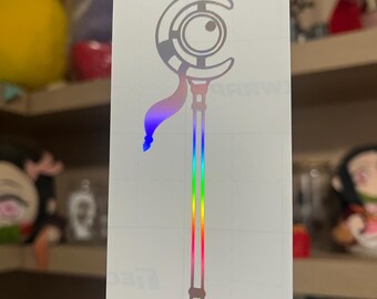 May include: A holographic vinyl decal featuring a vertical staff design with a crescent moon and circular eye motif at the top. The staff includes a flowing ribbon element and a long, straight handle, displaying a vibrant rainbow spectrum effect.