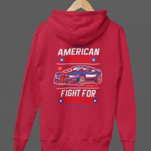 Op de afbeelding: Rode hoodie met een afbeelding van een blauwe en rode sportwagen. De tekst op de achterkant luidt "AMERICAN SPEED" en "FIGHT FOR FREEDOM". Het ontwerp bevat sterren en strepen.