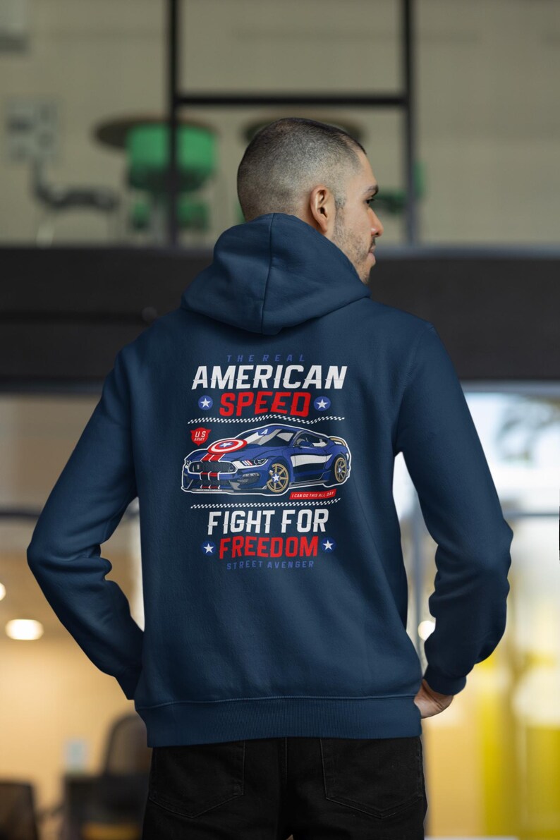Op de afbeelding: Marineblauwe hoodie met een afbeelding van een blauwe sportwagen en de tekst "AMERICAN SPEED" en "FIGHT FOR FREEDOM". Het ontwerp bevat rood, wit en blauw, wat een patriottisch thema oproept. De hoodie is een casual kledingstuk.