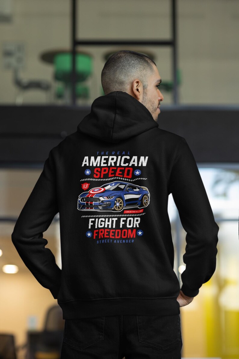 Op de afbeelding: Zwarte hoodie met een afbeelding van een blauwe sportwagen en de tekst "The Real American Speed" en "Fight for Freedom". Het ontwerp bevat rode, witte en blauwe elementen, die een patriottisch thema oproepen.