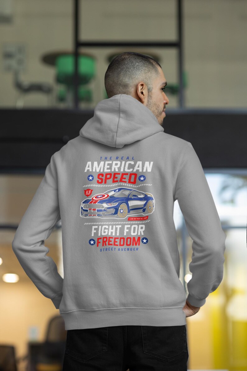 Op de afbeelding: Een grijze hoodie met een afbeelding op de achterkant. De afbeelding toont een blauwe en witte auto met de tekst "The Real American Speed" en "Fight for Freedom". De hoodie is een casual stijl.
