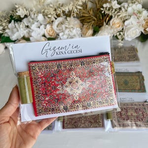 May include: A clear plastic package containing a small red and gold patterned rug-design pouch, a small glass bottle with a cork, and a card with the text "Gizem'in Kina Gecesi". Several similar packages are visible.