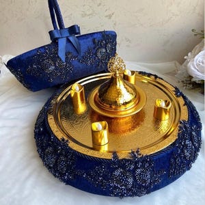 May include: A blue velvet tray with gold trim and a gold metal tea set with four candles. The tray is decorated with black beads and has a handle.