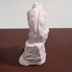 May include: A white ceramic sculpture of a frog sitting on a rock. The frog is in a seated position with its legs crossed and its head tilted down. The sculpture is detailed with textured surfaces and a smooth finish.