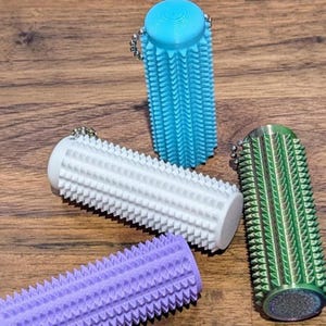 May include: Four colorful massage tools in blue, white, green, and purple. Each cylindrical tool has a textured surface with small, evenly spaced protrusions. The tools are designed with a keychain attachment.