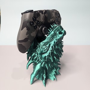 May include: A green dragon-shaped stand with a camouflage-patterned video game controller resting on its head.