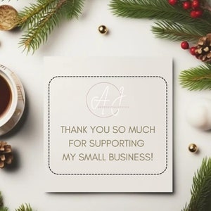 Puede incluir: Una tarjeta cuadrada con el texto "THANK YOU SO MUCH FOR SUPPORTING MY SMALL BUSINESS!" est&aacute; rodeada de vegetaci&oacute;n navide&ntilde;a, adornos dorados y una taza de t&eacute;. La tarjeta tiene un logotipo con las iniciales "AJ".