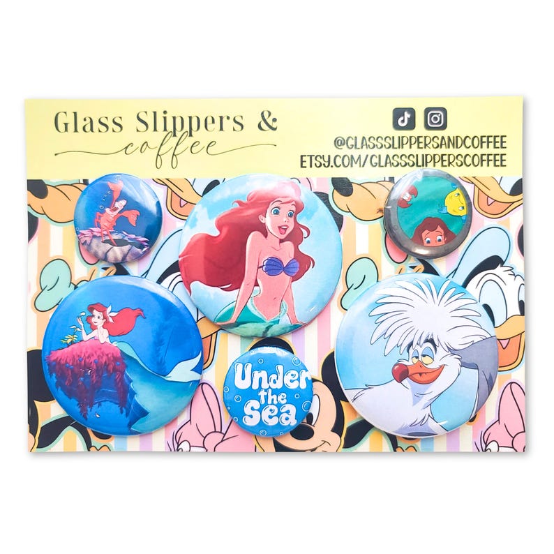 May include: A set of five circular pin-back buttons featuring characters and themes from The Little Mermaid, including Ariel, Sebastian, and Scuttle, displayed on a branded card with the text Glass Slippers & coffee and social media handles.