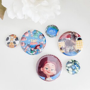 May include: A collection of six circular pin-back buttons featuring various designs. One button displays the Toy Story logo with characters, another shows a brown horse, one features a character with red hair, and others show patterns.