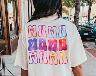 May include: A white t-shirt with a rainbow tie-dye design featuring the text "Mimi Mama Mimi" on the back.