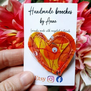 May include: A handmade heart-shaped brooch with yellow, orange, and red accents. The brooch is made with recycled materials and features the text "Handmade brooches by Anne". The Etsy logo is visible.