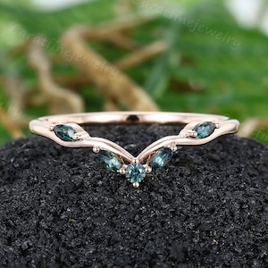 May include: A delicate rose gold wedding band with a V-shaped design featuring five marquise-shaped blue gemstones.