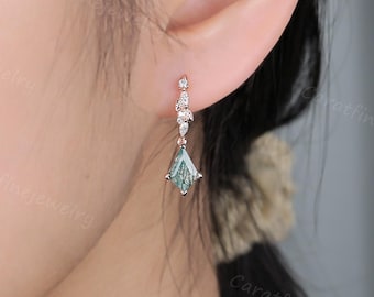 May include: A rose gold earring featuring a teal gemstone in a teardrop shape, complemented by small, clear accent stones. The earring hangs gracefully, showcasing a delicate design. The earring is displayed near an ear.