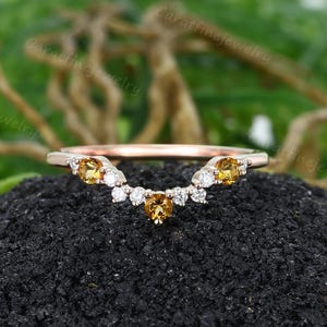 May include: A rose gold ring with a curved design, set with yellow and white gemstones. The ring has a delicate band and a series of small, sparkling stones set along the curve. The gemstones are a mix of yellow and clear, creating a beautiful contrast.