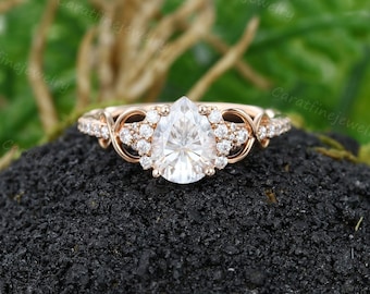 May include: A pear-shaped diamond engagement ring set in rose gold with a delicate, twisted band and a halo of smaller diamonds.