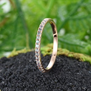 May include: A delicate rose gold band with a row of small, clear diamonds set in a pave setting. The band is thin and has a polished finish.