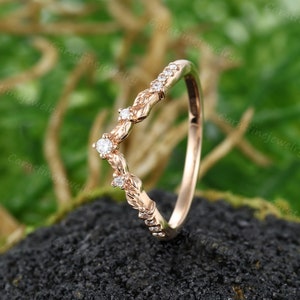 May include: A delicate rose gold wedding band with a V-shaped design featuring small diamonds and leaf accents.